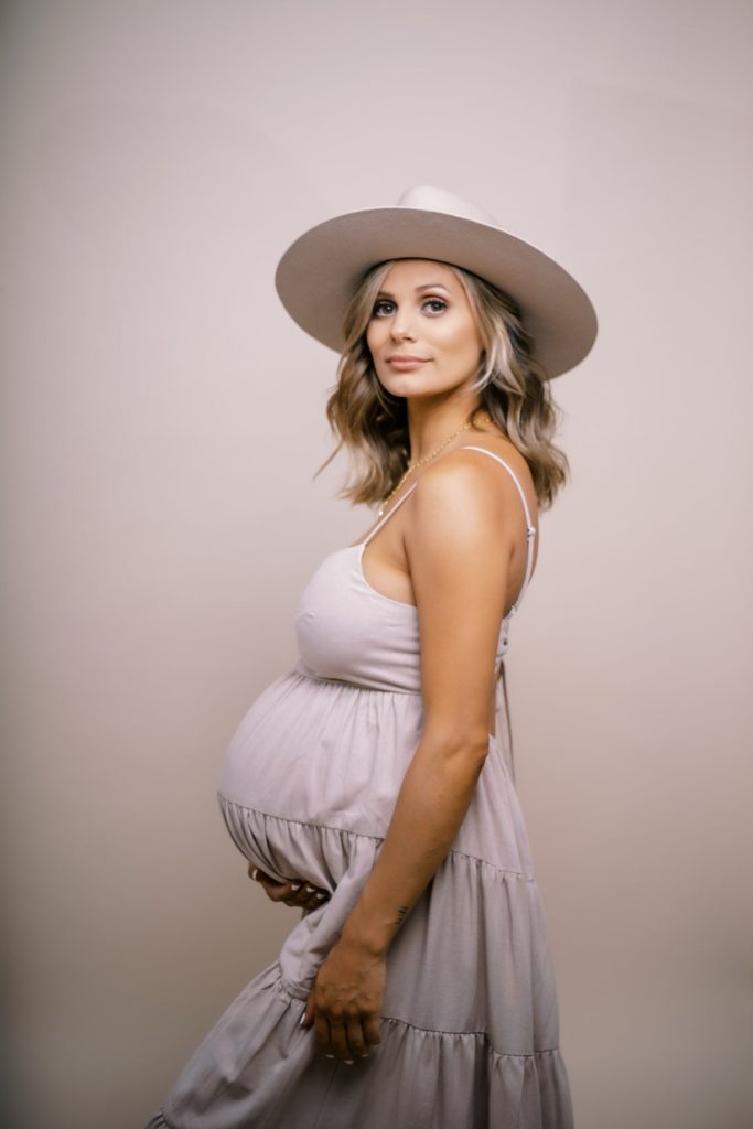 Maternity portrait of a woman in pink dress and tan colored suede hat