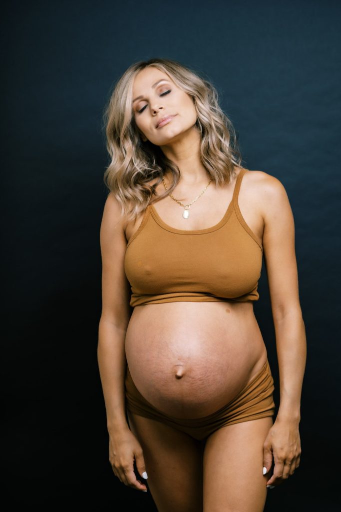 frontal portrait of a expecting mother as she points her face upward with hands to her side