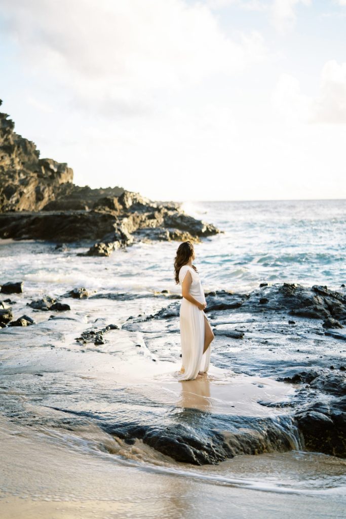 Young newly pregnant woman standing on a lava rock platform on a beach in Oahu, Hawaii