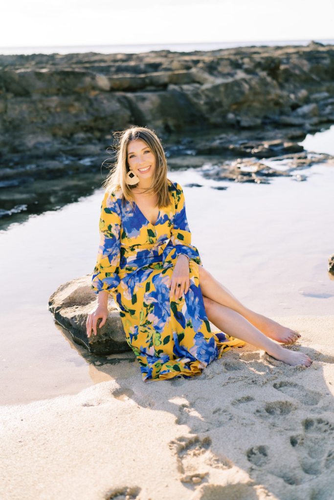 woman sitting on a rock at the beach in Hawaii wearing a floral flowy dress