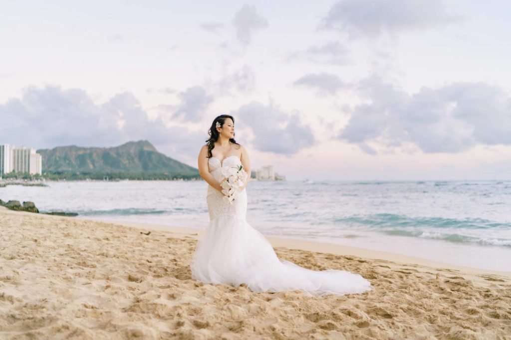 Bride in wedding dress looking away at The Halekulani Hotel Beach during sunset