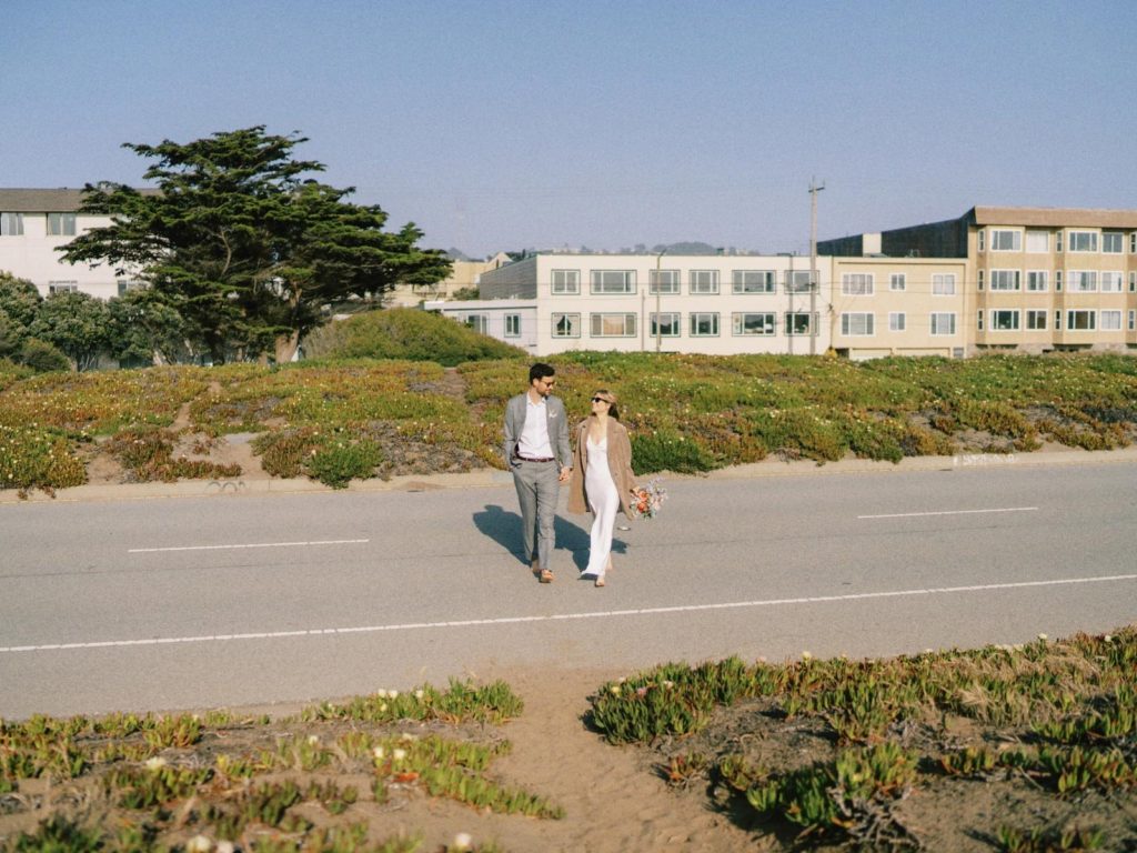 A wide view of houses in san francisco's outer sunset district with a couple crossing the street in wedding clothes