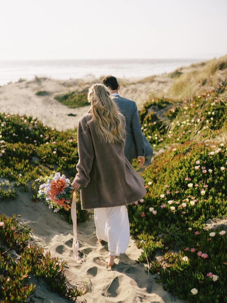 man and woman walking down the beach path while holding hands