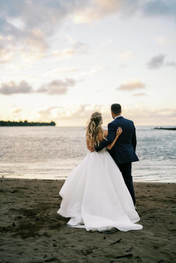 Newlyweds standing by the beach watching the sunset Intimate Elopement at Kualoa Ranch on Oahu