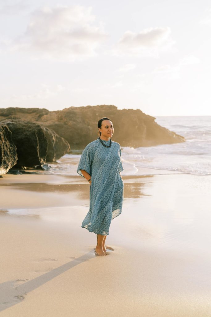 Woman wearing a blue dress looking towards the sunset in Waianae Beach Oahu Hawaii