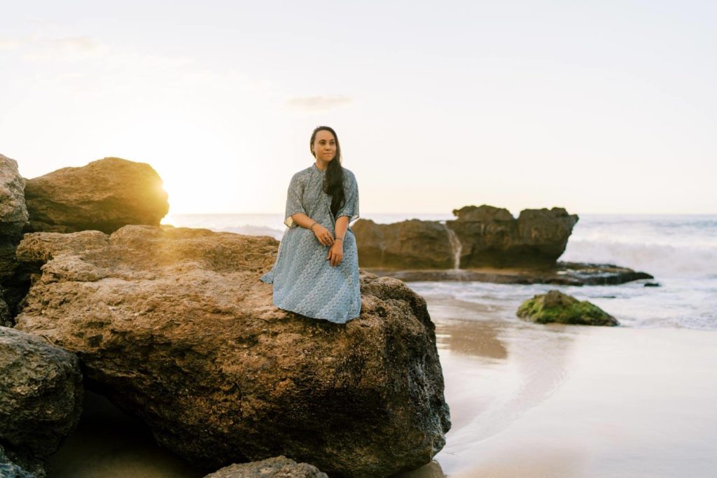 Woman sitting on the rocks next to the Waianae beach in Oahu Hawaii