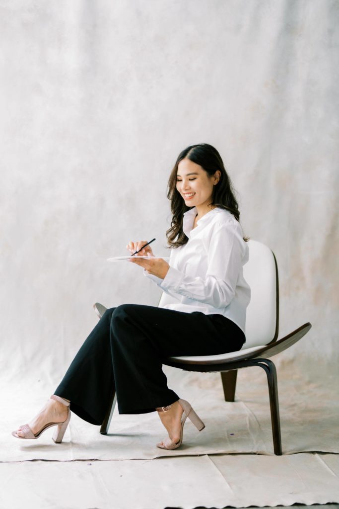 Photo of a Woman in white shirt and black trousers smiling while holding her color palette a branding session