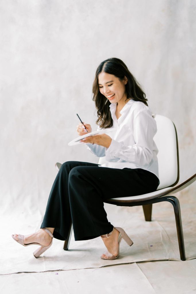 Photo of a Woman in white shirt and black trousers smiling while holding her color palette a branding session