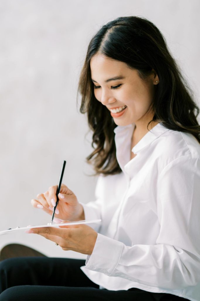 Photo of a Woman in white shirt and black trousers smiling looking at her color palette a branding session