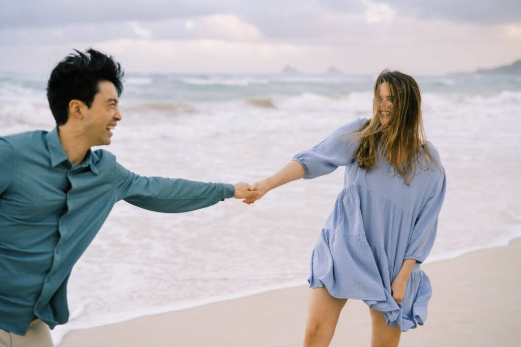 Couple happily pulling each other by the beach engagement session