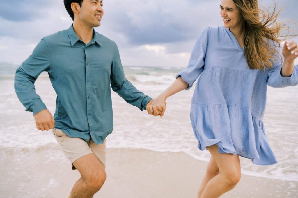 Photo of Newly engaged couple chasing each other at the beach