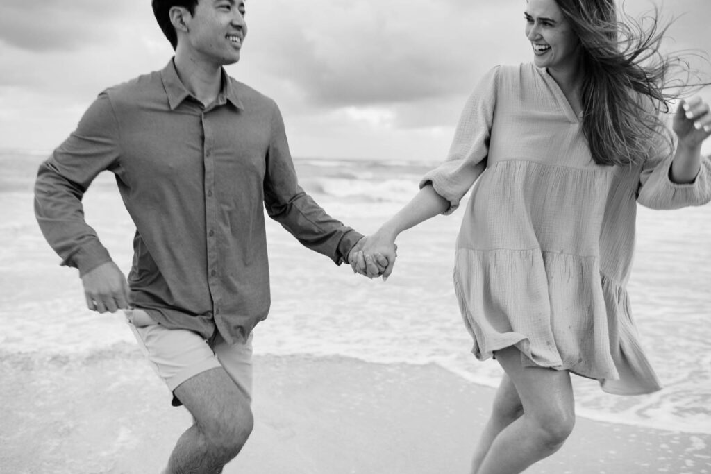 Black and White photo of Newly engaged couple chasing each other at the beach