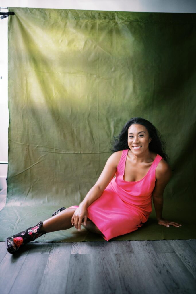 Woman sitting on the floor wearing a bright pink dress smiling vibrantly 