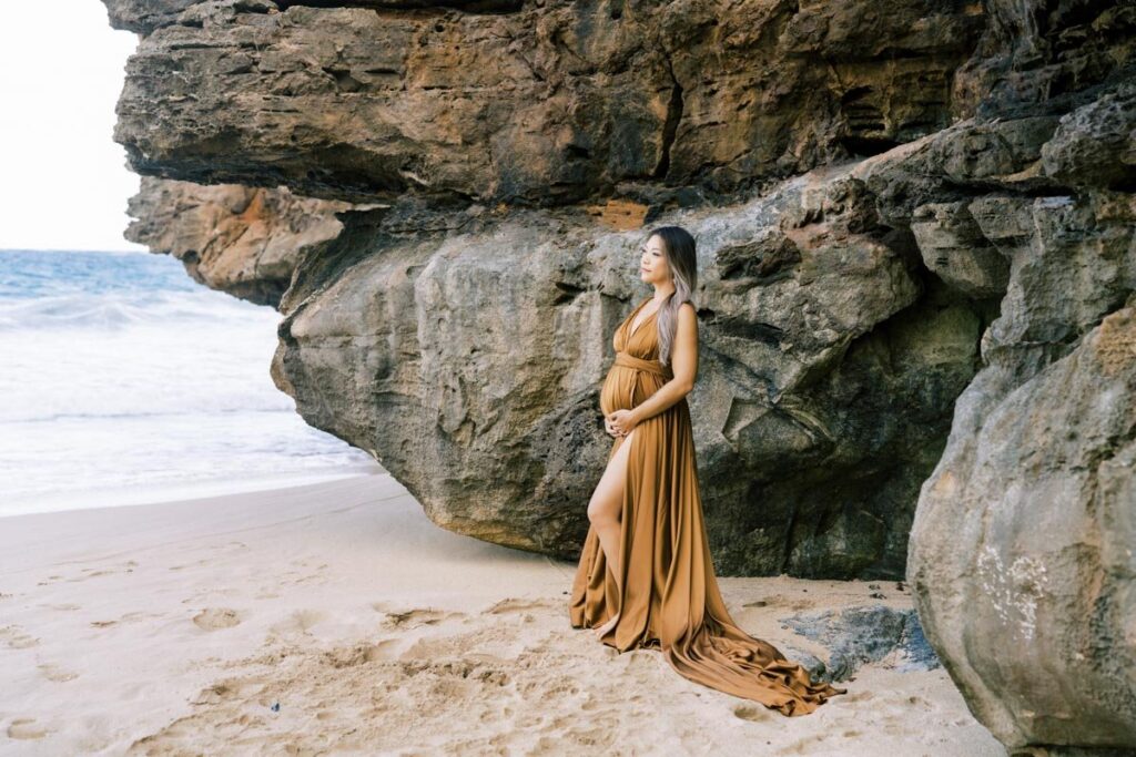 North Shore Maternity Photos of a pregnant woman holding her baby bump wearing a brown dress at Laie beach