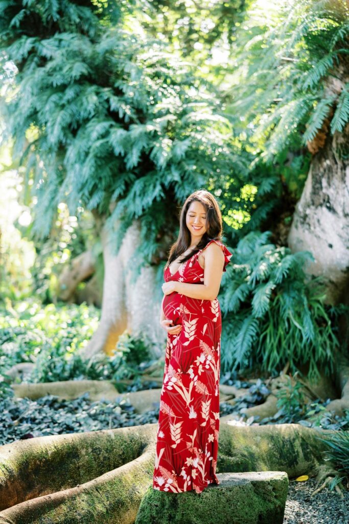 A Pregnant woman wearing a long red floral dress on her Pregnancy Photo Session at Oahu Botanical Garden