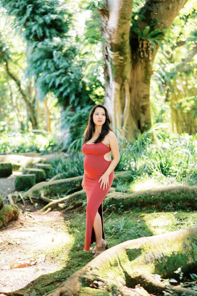 A Pregnant woman wearing a red bodycon dress on her Maternity Photo Session at Oahu Botanical Garden