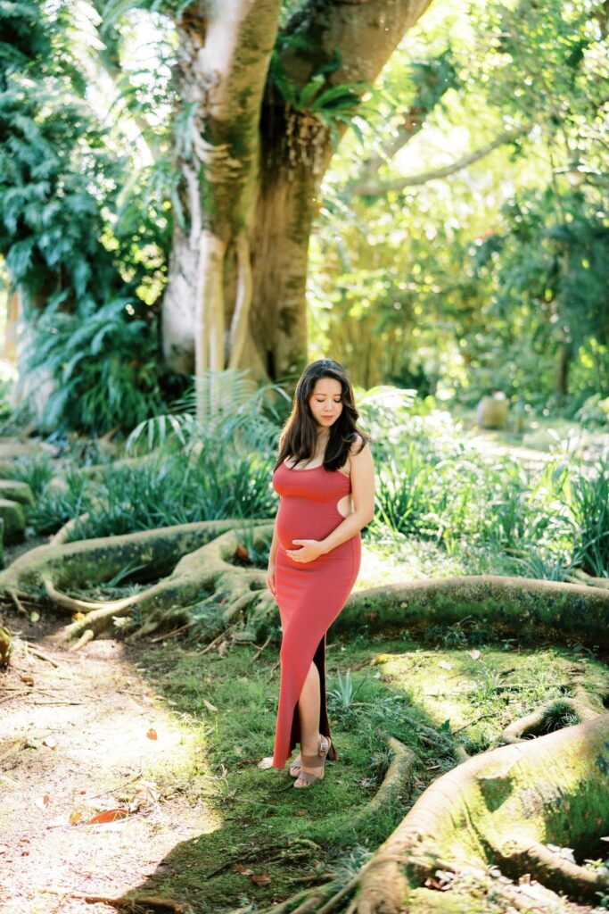 A Pregnant woman wearing a red bodycon dress on her Pregnancy Photo Session at Oahu Botanical Garden