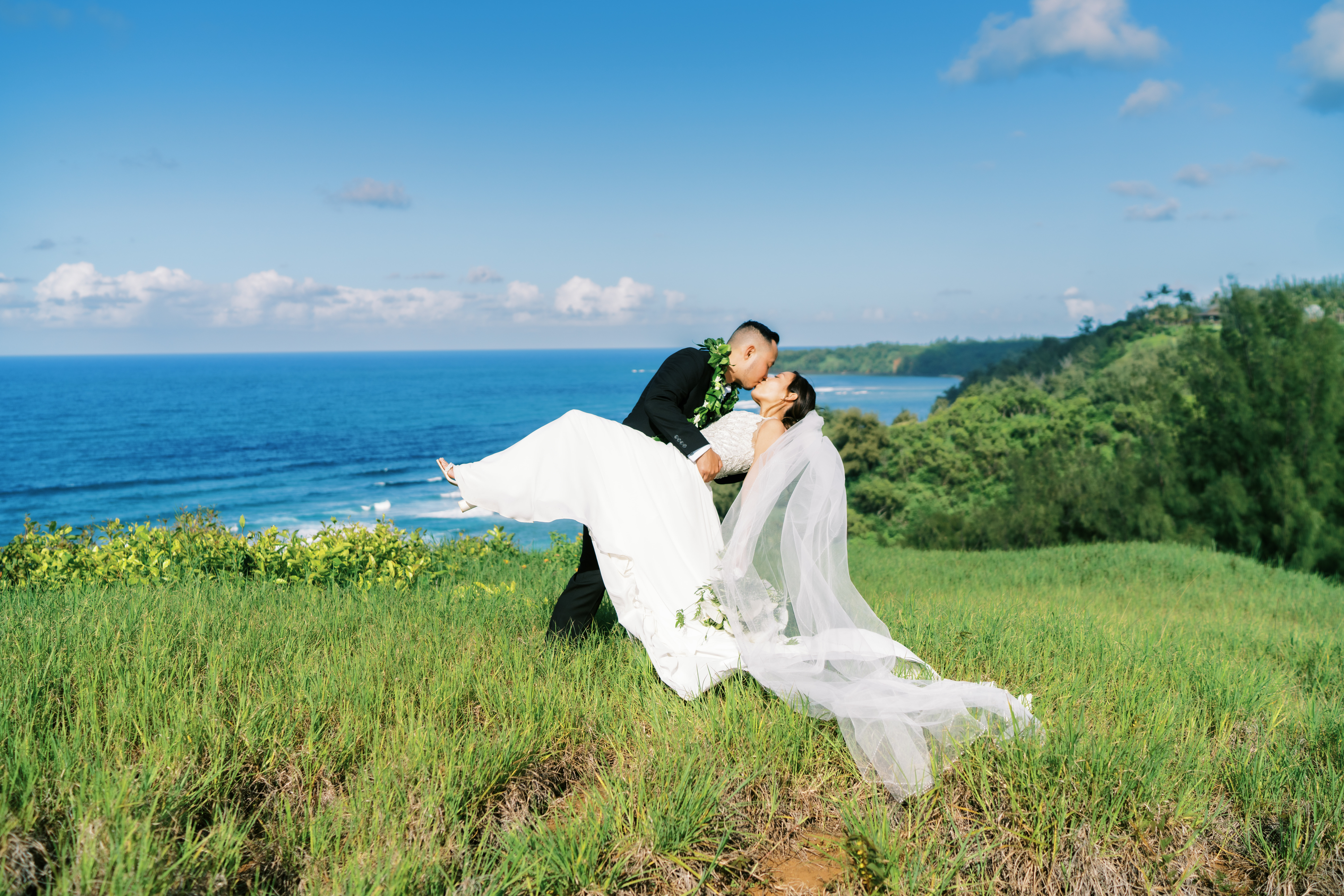 Bride and groom sharing a kiss on a lush coastal hillside captured by Oahu wedding photographer
