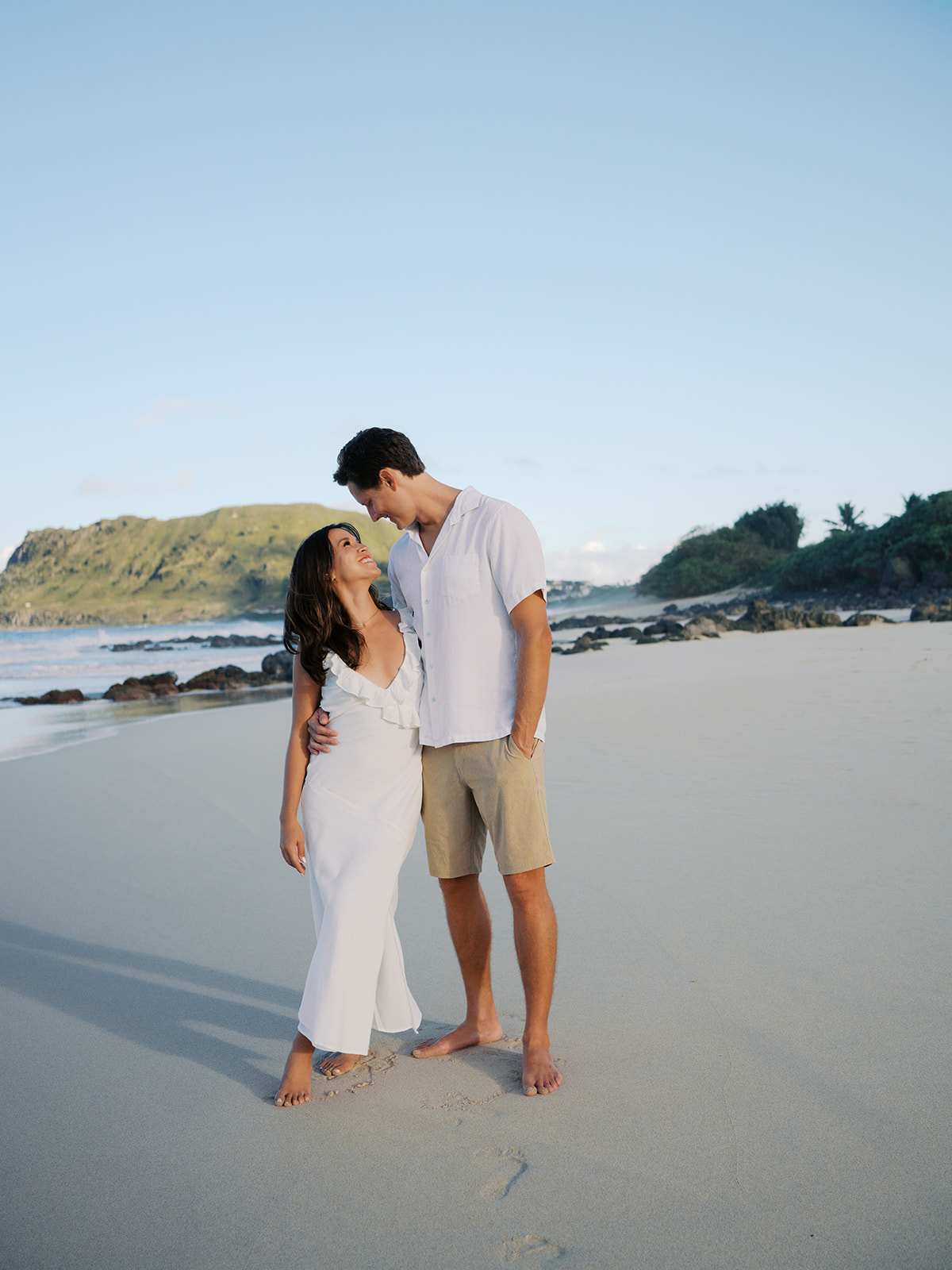 Couple standing on the sand of a beach in Hawaii with their arms around eachother