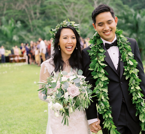 Smiling bride and groom wearing traditional Hawaiian maile leis after their Honolulu wedding ceremony.